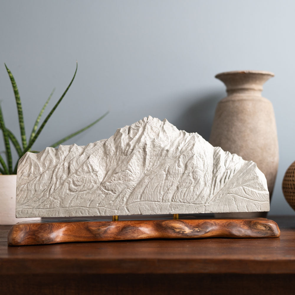 Hand carved stone sculpture of Pioneer Peak displayed on a table next to a vase and a plant.