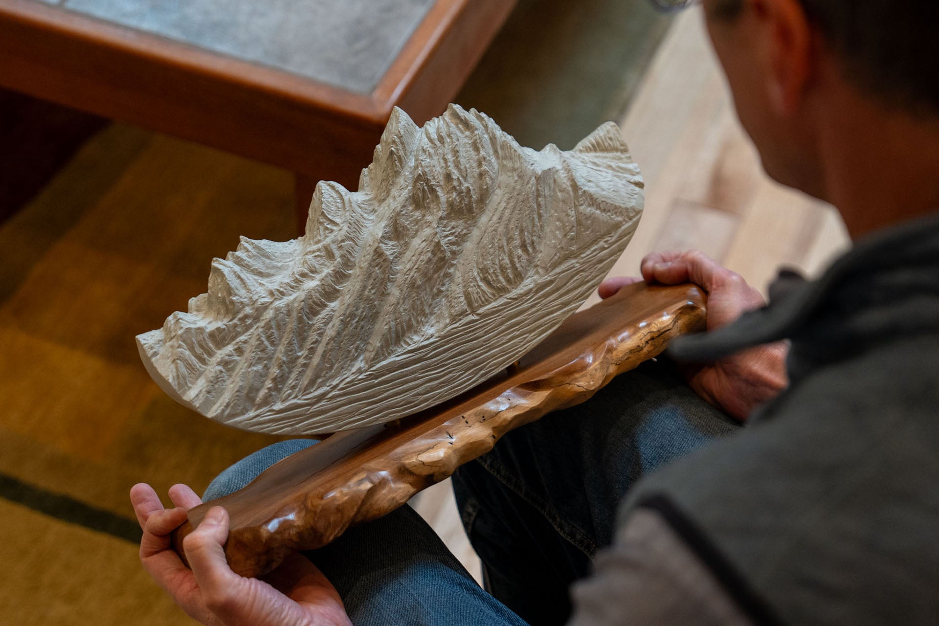 A person holding a large Grand Teton sculpture on a rustic wood base in a warmly lit setting.