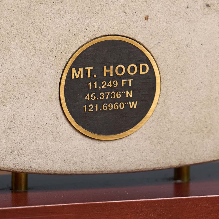 Close-up of a brass medallion engraving on a Mt. Hood sculpture, displaying the mountain's elevation and GPS coordinates.